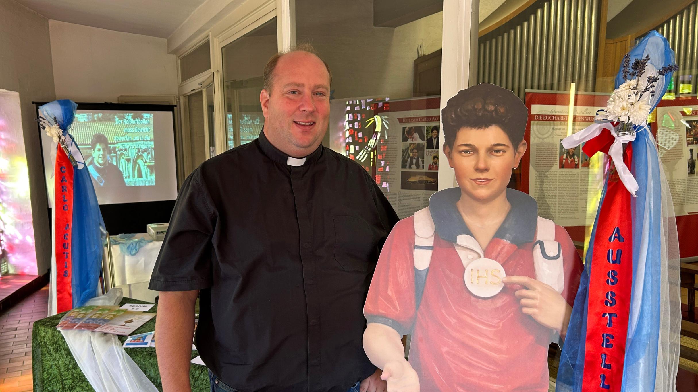 Pfarrer Lars Meiser mit einem lebensgroßen Aufsteller des Heiligen Carlo Acutis im Eingangsbereich der Klosterkirche.